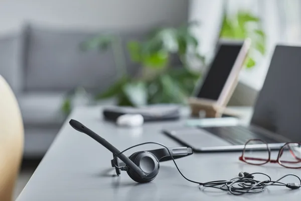 Close-up of a modern workspace featuring a headset, laptop, and plants.