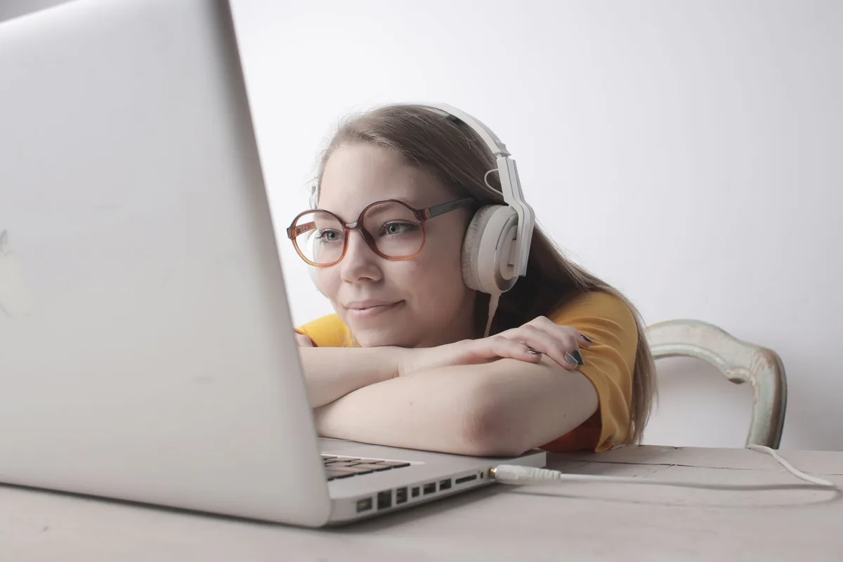 Smiling woman wearing headphones and glasses, relaxing with a laptop indoors.