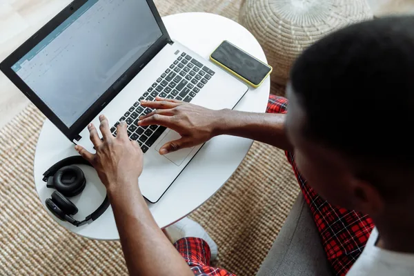 Top view of a man typing on a laptop, with a smartphone and headphones on the desk.