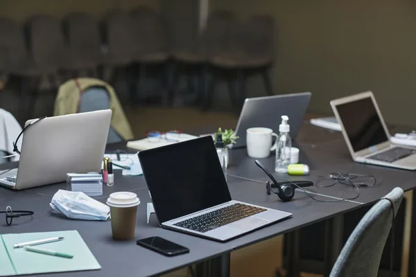 A cluttered office desk setup featuring multiple laptops, coffee cup, and office supplies for a busy workday.