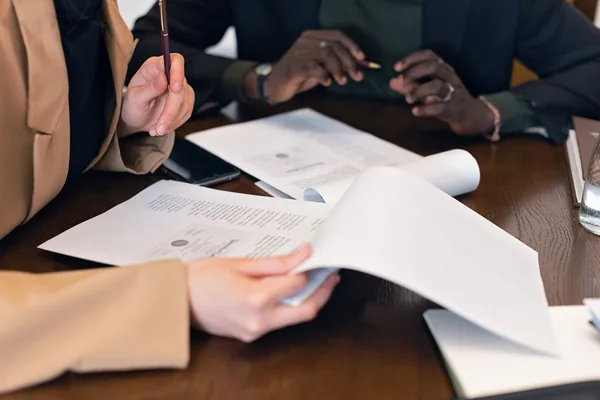 Close-up of professionals reviewing documents during a business meeting in an office setting.