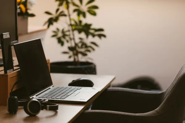 A cozy home office workspace with a laptop, headphones, and a plant. Ideal for remote work.