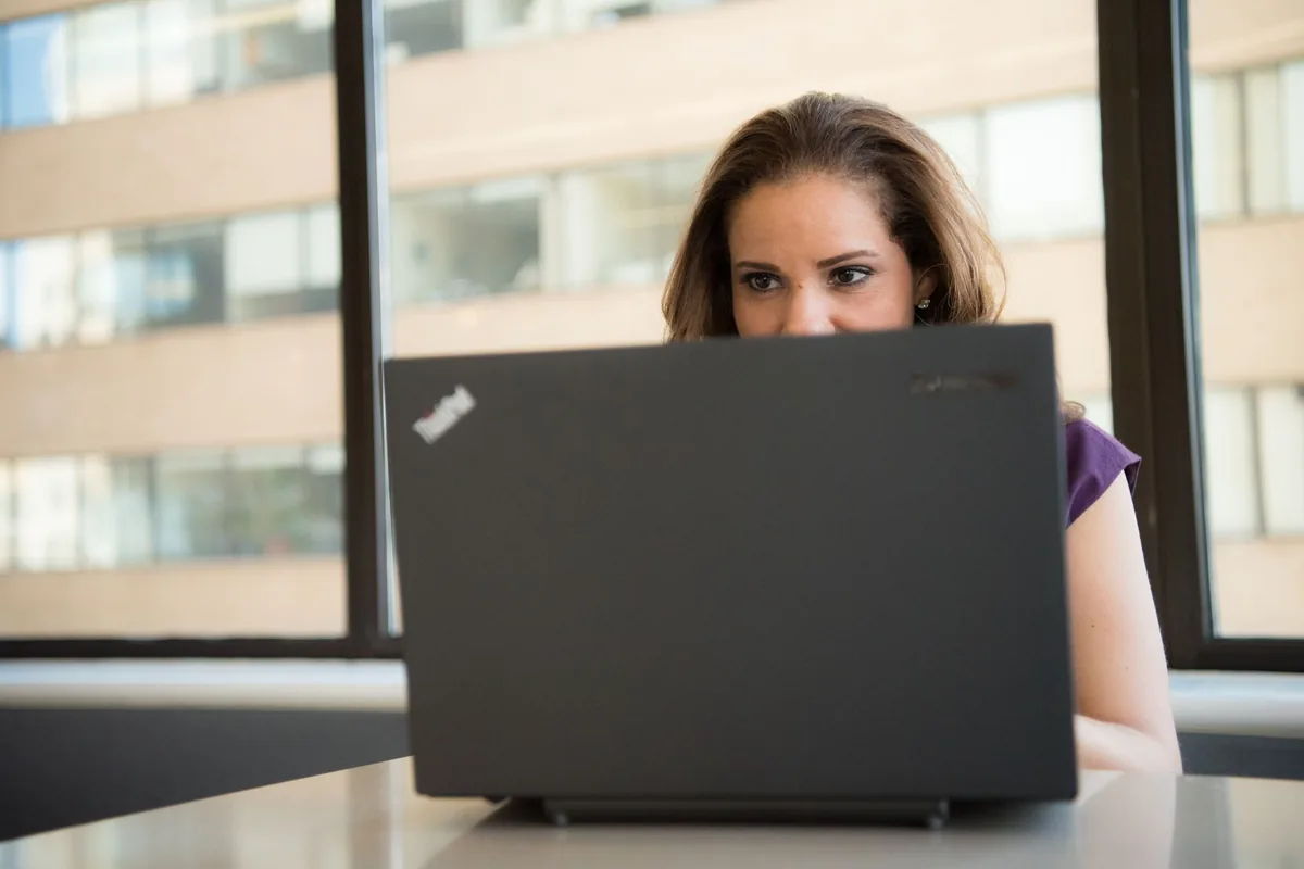 Focused woman using a laptop in a brightly lit office setting, showcasing modern work technology.
