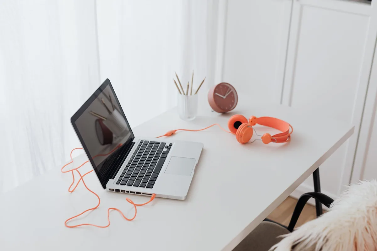 Minimalist workspace featuring a laptop and orange headphones on a clean white desk.