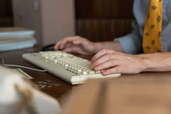 Adult male working on a computer with coins and paperwork nearby.