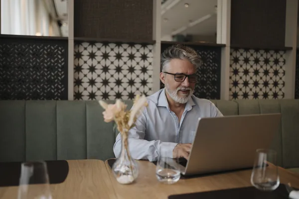 An older man working on a laptop in a cafe