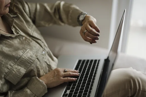 A person typing on a laptop at home while checking the time