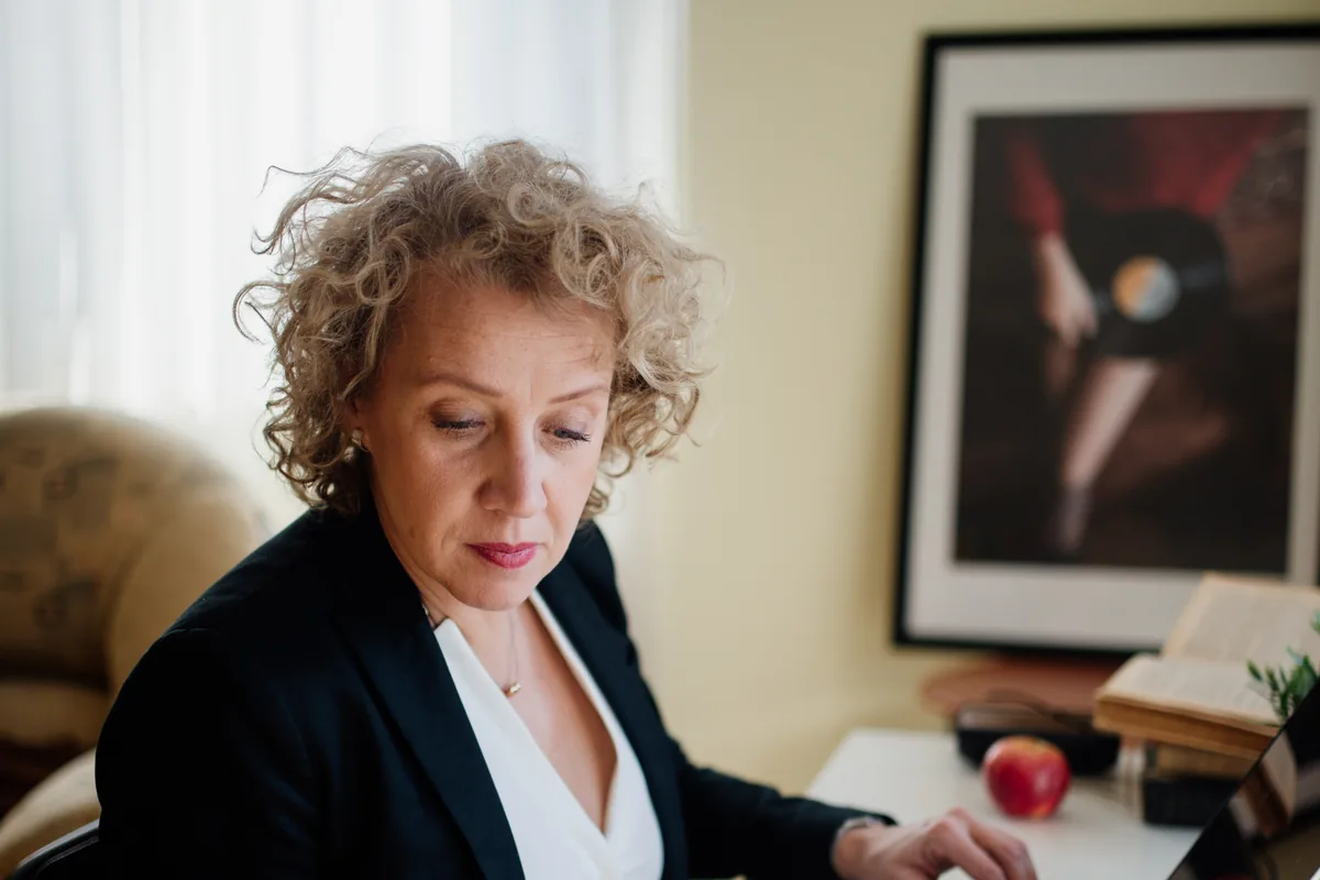 A person working at a desk with a laptop and paper documents in a bright office