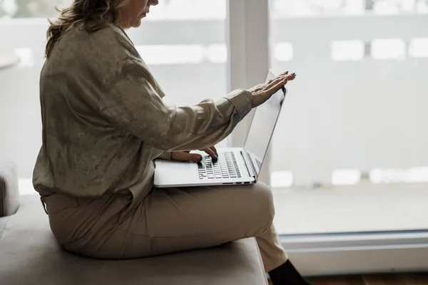 A person working on a laptop beside a window