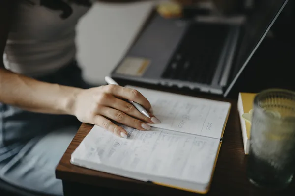 A person taking notes while using a laptop at a desk