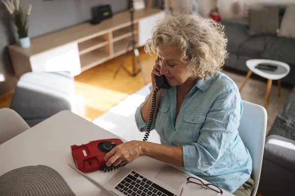 A person talking on a phone while working on a laptop in a living room