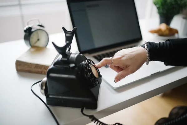 A hand on a desk telephone next to a laptop