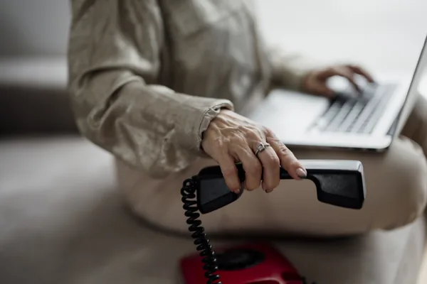 A person using a laptop while holding a telephone receiver